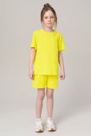 Girl wearing bright yellow short-sleeve t-shirt and shorts set, white sneakers, studio background