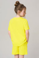 Girl in bright yellow short-sleeve tee and shorts, standing with hands in pockets