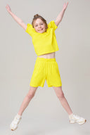 Smiling girl jumping in yellow summer activewear tee and shorts, white sneakers
