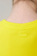 Back neck view of a girl wearing a bright yellow athleisure tee with logo patch