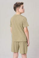 Boy wearing light olive short-sleeve t-shirt and matching shorts, back view, neutral background