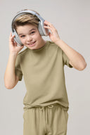 Boy in light green athleisure set and headphones, smiling against plain background