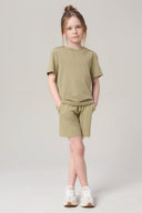 Girl wearing light olive green athleisure t-shirt and shorts set with white sneakers.