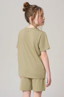 Girl wearing light olive green basic tee and matching shorts, back view, neutral background