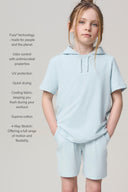Girl in light blue hooded athleisure tee and shorts, standing against a neutral background.