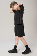 Boy wearing charcoal hooded tee and black athletic shorts, side view, neutral background