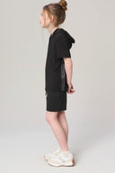 Girl in charcoal hooded tee and shorts, side pose, wearing white sneakers, neutral background