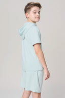 Boy in light blue short-sleeve hooded tee and shorts, side view, neutral background