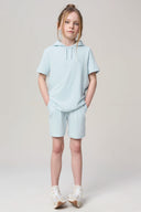 Girl wearing light blue hooded tee and shorts set, hands in pockets, casual sporty look
