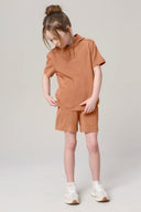 Girl wearing mocha brown hooded short-sleeve tee and matching shorts, standing indoors
