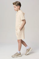 Boy wearing a sand-colored hooded tee and athletic shorts in studio, side view