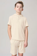 Boy wearing sand-colored short sleeve hooded tee and matching shorts, neutral background