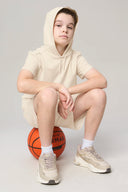 Boy in sand-colored hooded tee and shorts posing with basketball, athleisure style
