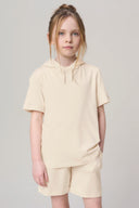Girl wearing sand-colored hooded short sleeve tee and matching shorts, neutral background