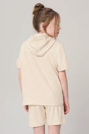 Girl in sand-colored hooded tee and shorts, back view, neutral background