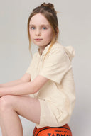 Girl in sand-colored hooded tee and shorts sitting on basketball, athleisure apparel