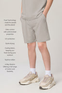 Boy wearing driftwood-colored relaxed shorts with side pockets, white socks, and beige sneakers