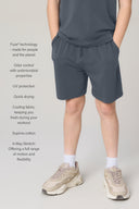 Boy wearing granite relaxed shorts, hands in pockets, with athletic sneakers, light background