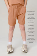 Boy wearing relaxed fit mocha athletic shorts with drawstring, hands in pockets, neutral backdrop