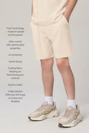 Boy wearing sand-colored relaxed athletic shorts with side pockets, white socks, and beige sneakers, showcasing comfort and movement.