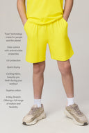 Boy wearing bright yellow relaxed fit athletic shorts, Supima cotton, neutral sneakers.