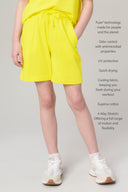 Girl wearing bright yellow relaxed shorts with drawstring waist, hands in pockets, white sneakers