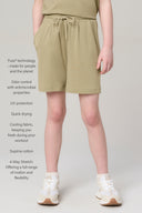Girl wearing light olive relaxed athletic shorts with drawstring waist and white sneakers.