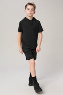Boy in charcoal athletic shorts and black hooded t-shirt walking in studio