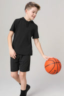 Boy in charcoal athletic shorts and black hoodie shirt dribbling basketball indoors
