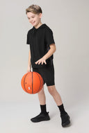 Boy in charcoal athletic shorts and black hoodie dribbling basketball indoors