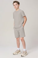 Boy wearing neutral driftwood athleisure shorts and t-shirt set, hands in pockets