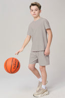 Boy in neutral activewear t-shirt and shorts playing basketball indoors