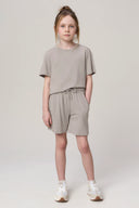 Girl wearing neutral driftwood shorts and matching t-shirt athleisure set, standing indoors