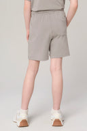 Back view of girl wearing driftwood beige athletic shorts, casual top, and white sneakers