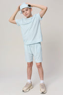Boy in light blue athleisure shorts, t-shirt, cap and sneakers on neutral background