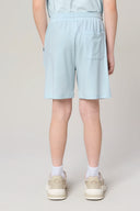 Boy wearing light blue athletic shorts with back pocket, white socks, and beige sneakers
