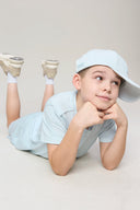 Boy in light blue athleisure shorts and cap lying on floor in casual pose