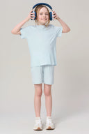 Girl in light blue activewear shorts and t-shirt, wearing headphones, standing indoors