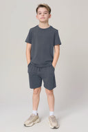 Boy in granite gray athletic t-shirt and shorts set, hands in pockets, studio background