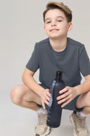 Boy in granite gray athletic shorts and t-shirt, holding a water bottle, neutral background