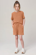 Girl wearing mocha-colored athleisure shorts and t-shirt set, standing against a plain background