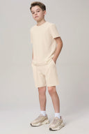 Boy wearing sand-colored athletic shorts and t-shirt set with beige sneakers, studio background
