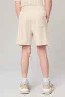 Boy wearing beige athleisure shorts with elastic waistband and back pocket, rear view