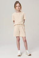 Girl wearing sand-colored athleisure t-shirt and shorts, standing in studio, white sneakers