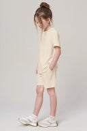 Girl in sand-colored athleisure shorts and t-shirt with white sneakers, neutral background