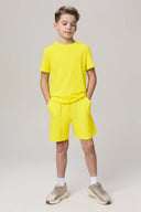 Boy in bright yellow short-sleeve t-shirt and shorts, athleisure summer outfit, neutral background