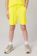 Boy wearing bright yellow athletic shorts with drawstring waist, beige sneakers, and white socks