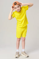 Boy in yellow activewear t-shirt and shorts, tan sneakers, orange cap, studio background