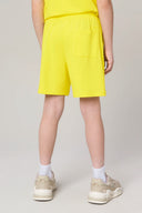 Boy wearing yellow athletic shorts and sneakers, rear view, neutral background