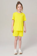 Girl in bright yellow short-sleeve athleisure set and sneakers on light background